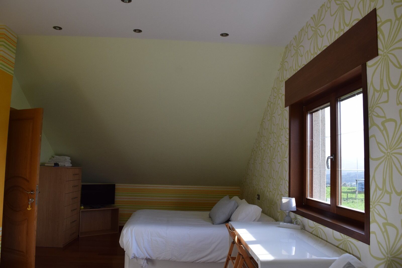 Une chambre avec deux lits, une armoire en bois, un téléviseur posé sur un meuble et une fenêtre donnant sur un paysage verdoyant.