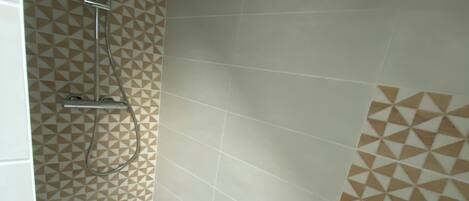 A shower area with a geometric patterned wall, a handheld showerhead, and a wall-mounted faucet.