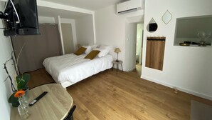 A bedroom with a bed, bedside table, lamp, and an air conditioning unit. - Studio chic l'Auvétia (Arnage)