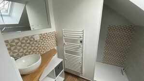 A modern bathroom with a skylight, a white sink, a wooden vanity, and a towel rack. - Studio chic l'Auvétia (Arnage)
