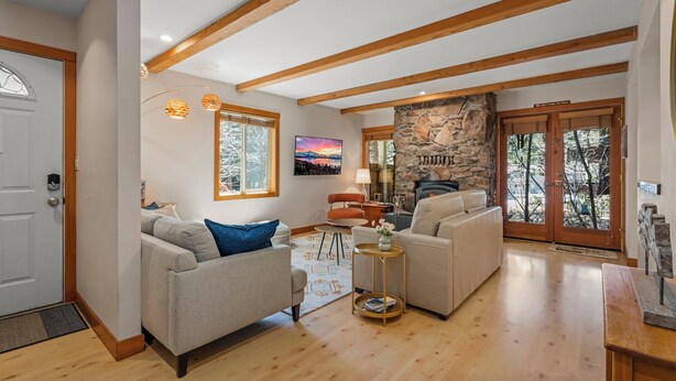 A spacious living room with wooden beams, a stone fireplace, and a large window with a view of trees.