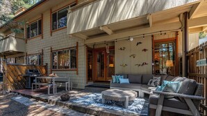 A two-story house with a covered porch, a grill, a sofa, and a dining table.