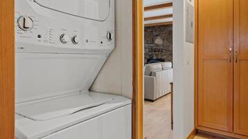 A laundry room with a front-loading washer and dryer, wooden cabinets, and a stone wall in the background.