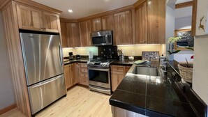 A kitchen with wooden cabinets, stainless steel appliances, a black countertop, and a tiled backsplash.