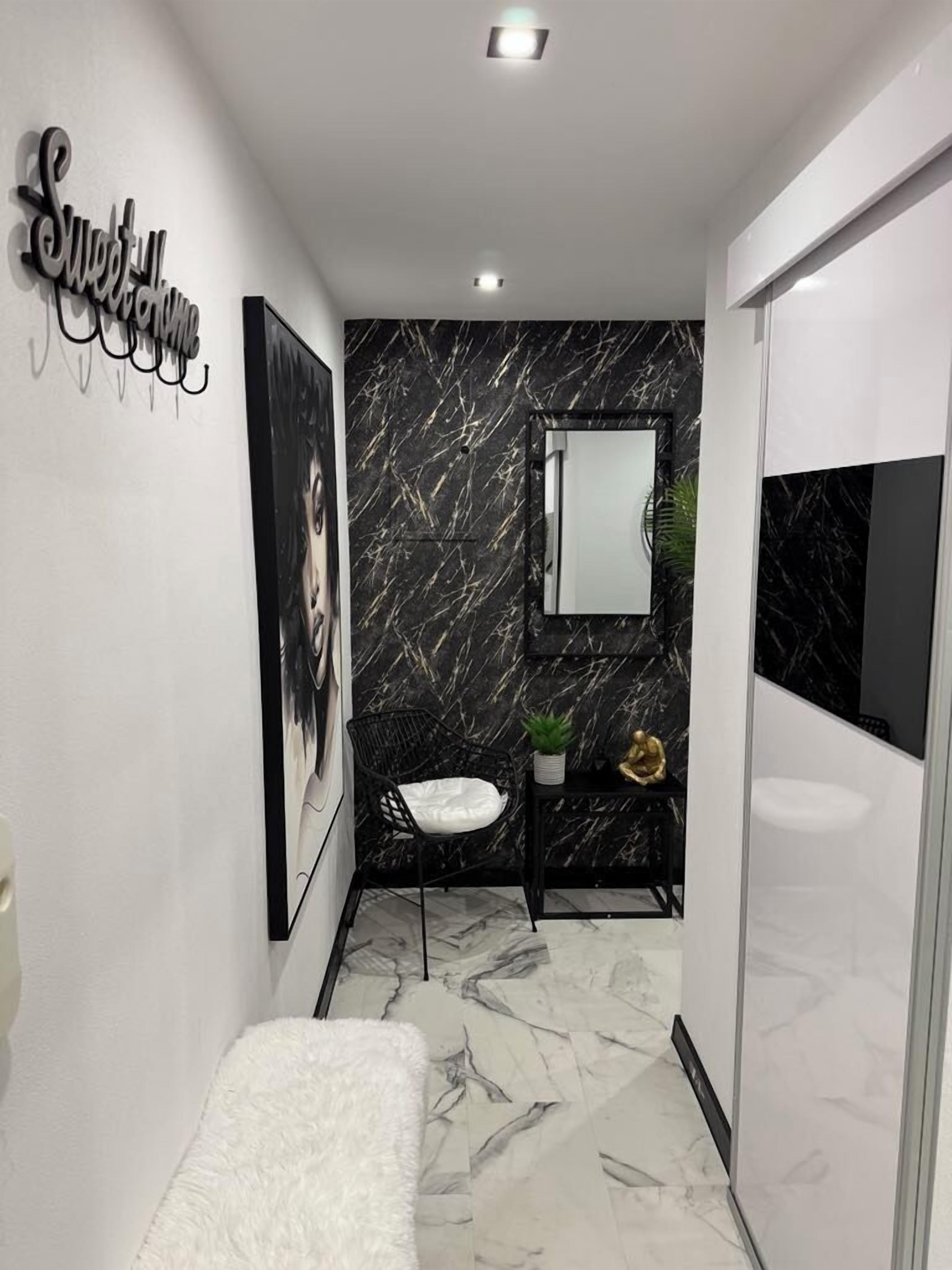 Une salle de bain moderne avec un sol en marbre, un mur en marbre noir et blanc, un lavabo, un miroir, une chaise noire et une serviette blanche.