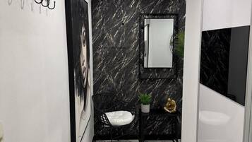 Ein modernes Badezimmer mit Marmorboden, einer Wand aus Schwarz-Weiß-Marmor, einem Waschbecken, einem Spiegel, einem schwarzen Stuhl und einem weißen Handtuch.