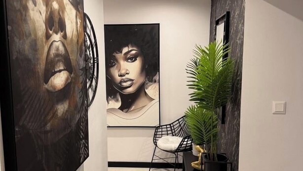 Un couloir doté d’un sol en marbre, deux grandes peintures abstraites, une chaise noire et une plante en pot.