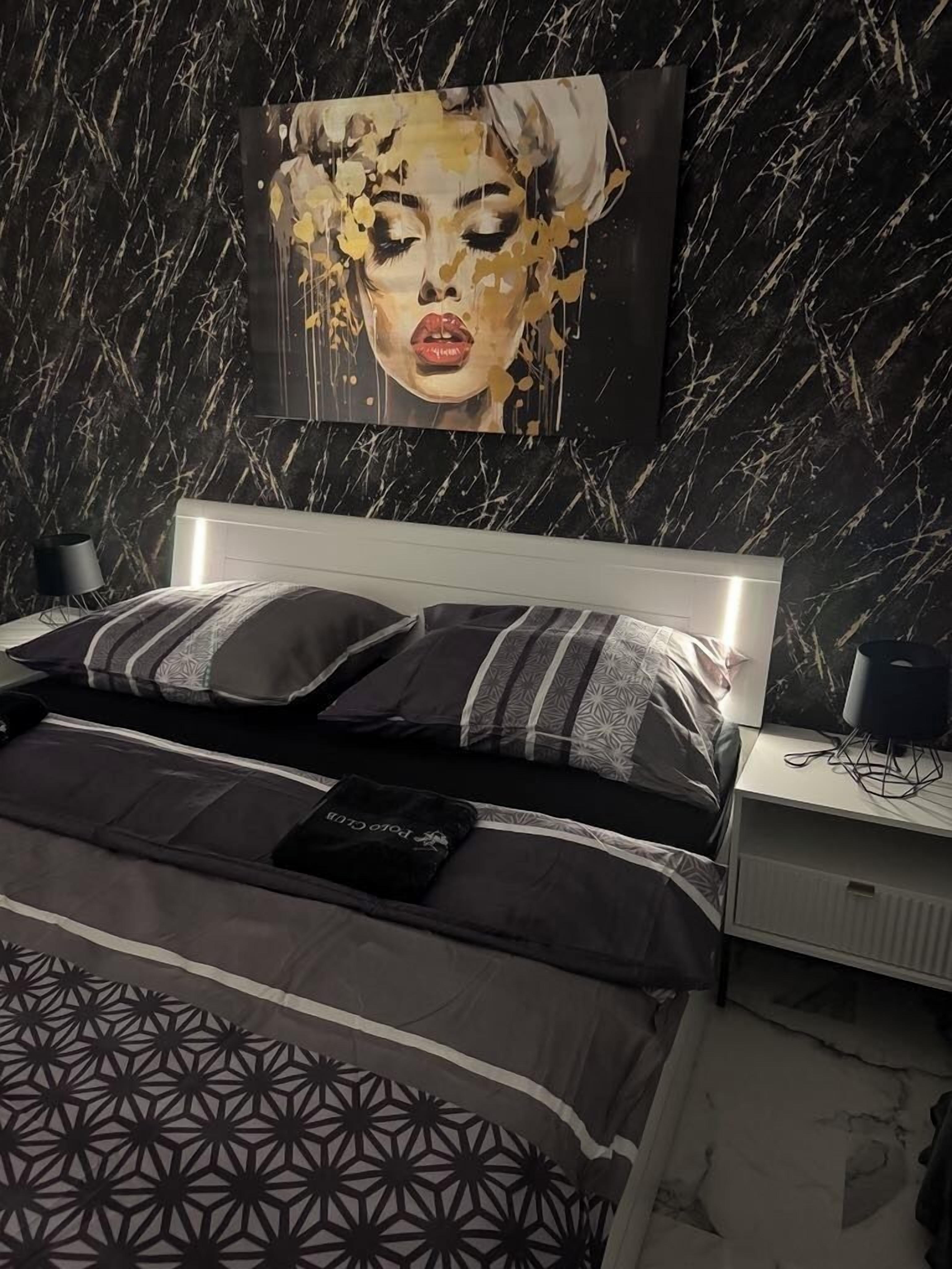 A modern bedroom with a marble-patterned wall, a large bed with patterned bedding, and a headboard with integrated lighting.