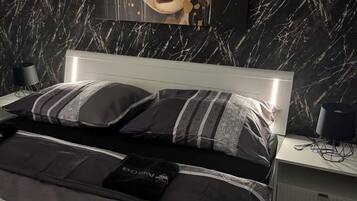 A modern bedroom with a marble-patterned wall, a large bed with patterned bedding, and a headboard with integrated lighting.