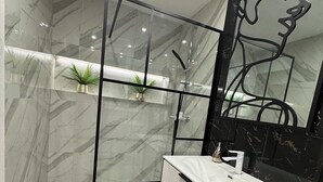 Une salle de bain moderne avec une paroi en verre, des murs en marbre, un meuble-lavabo blanc et un grand miroir.