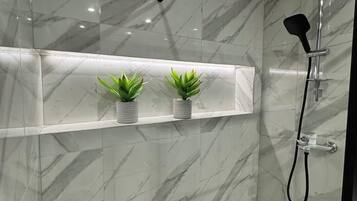 Une salle de bain moderne avec une douche à parois de verre, des murs en marbre et deux plantes en pot disposées sur une étagère.