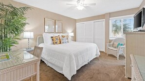 A bedroom with a bed, a ceiling fan, a window, a television, and a plant. - 2BR Condo Sleeps 6 – Pool & Steps to the Beach (Panama City Beach)