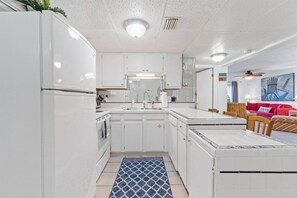 A compact kitchen with white cabinets, a central island, and a dining area with a red sofa. - 2BR Condo Sleeps 6 – Pool & Steps to the Beach (Panama City Beach)