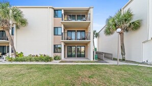 A multi-story residential building with balconies, a well-maintained lawn, and palm trees. - 2BR Condo Sleeps 6 – Pool & Steps to the Beach (Panama City Beach)