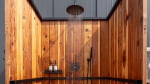 Un cerramiento de ducha de madera con ducha de lluvia, cabezal de ducha manual y estante con artículos de tocador.