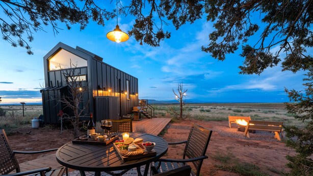 Una cabaña rústica con terraza, mobiliario exterior y una chimenea al aire libre.