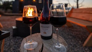 Una botella de vino Meomi Pinot Noir y dos copas sobre un tocón de madera.