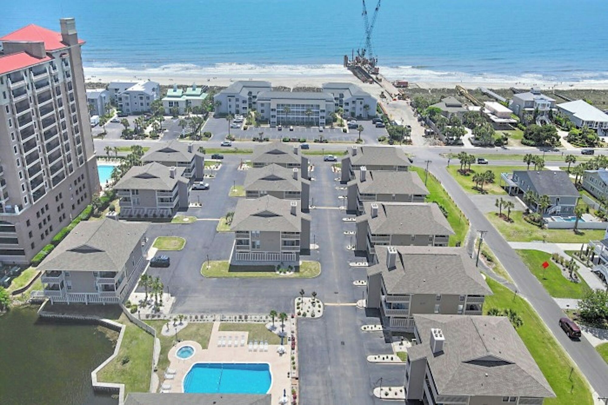 Ein Wohngebiet mit zentralem Pool, mehreren Gebäuden und einem Strand im Hintergrund.