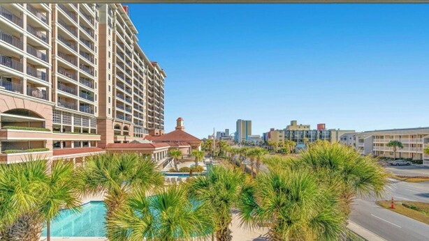A high-rise hotel with multiple balconies, a swimming pool, and a cityscape in the background. - Tilghman Lakes C4- 2BR/2BA- 2nd Row, Pool (North Myrtle Beach)
