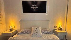 A bedroom with a bed, two bedside tables, a nightstand, a wall-mounted artwork of lips, and two wall-mounted lamps. - Calanegra Apartment with Private Pool - Ground Floor - Puerto de Mazarrón (Mazarrón)