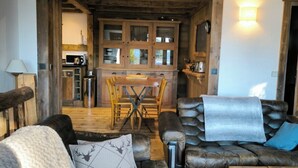 A rustic living room with a leather sofa, a wooden coffee table, and a dining area with a wooden table and chairs. - Apartment in residence near the Mont d'Arbois (Megève)