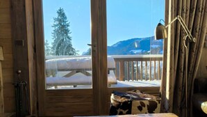 A wooden cabin room with a large window, a wooden table, and a cowhide cushion. - Apartment in residence near the Mont d'Arbois (Megève)