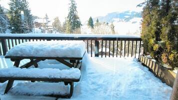 Una terraza de madera con una mesa de picnic y bancos cubiertos de nieve.