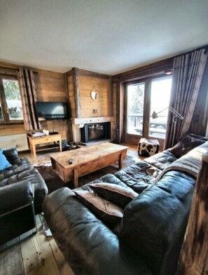 A cozy living room with a wooden interior, a fireplace, a television, and a leather sofa.