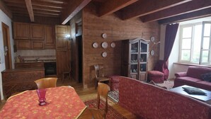 A rustic interior with wooden beams, a dining table with a patterned tablecloth, a red sofa, and a cabinet with decorative plates. - Apartment with fireplace near the Vauban City (Briançon)