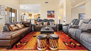 Un salon spacieux avec un canapé en cuir marron, des fauteuils gris et un tapis à motifs.