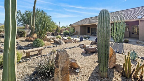 Un jardin désertique avec des cactus et des rochers, un banc et un bâtiment doté d’un toit en tuiles.