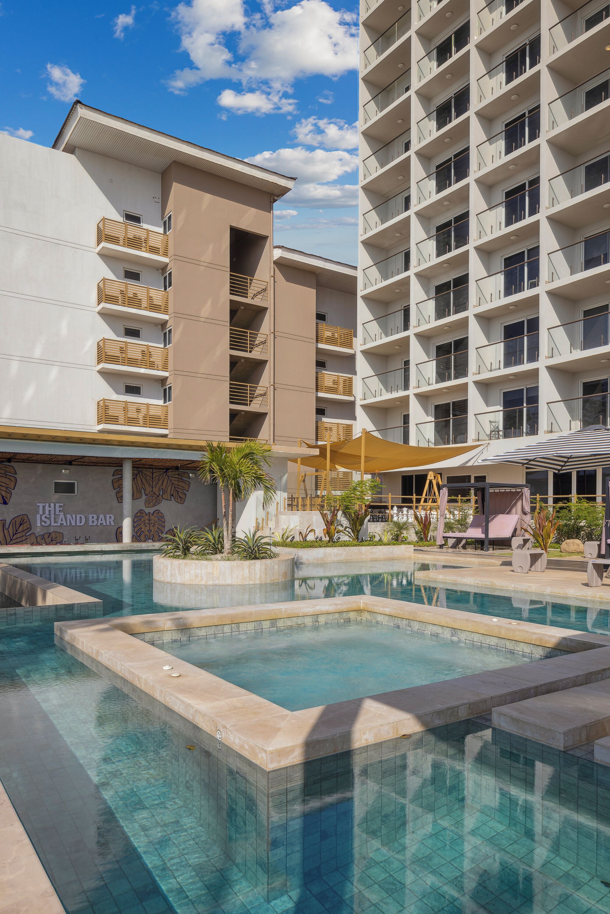 Un hotel con piscina, un bar llamado "The Island Bar" y un edificio de varios pisos con balcones.