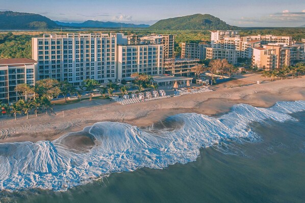 A beachfront hotel with multiple buildings, a sandy beach, and ocean waves.