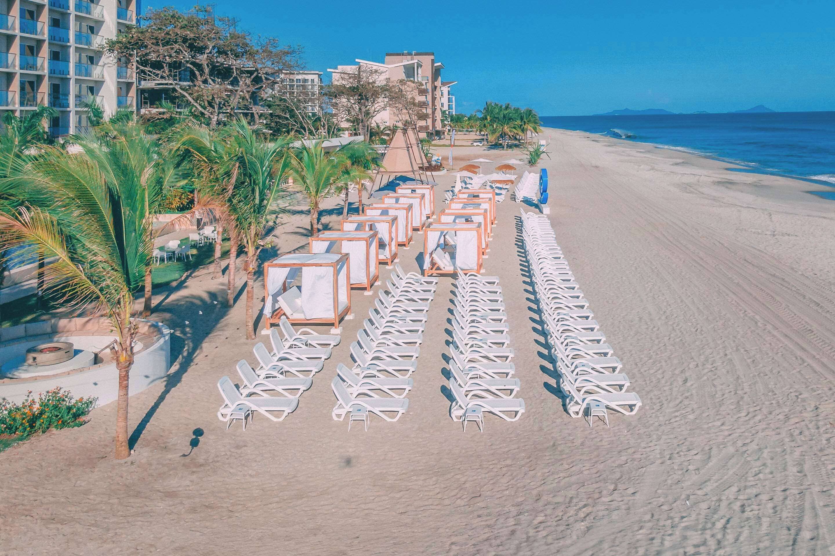 Un hotel frente a la playa con filas de tumbonas y una zona de piscina.