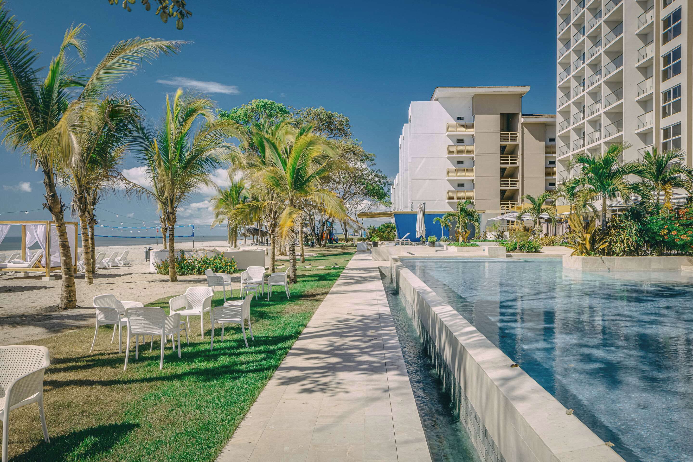 A pool area with lounge chairs and palm trees, adjacent to a high-rise building.
