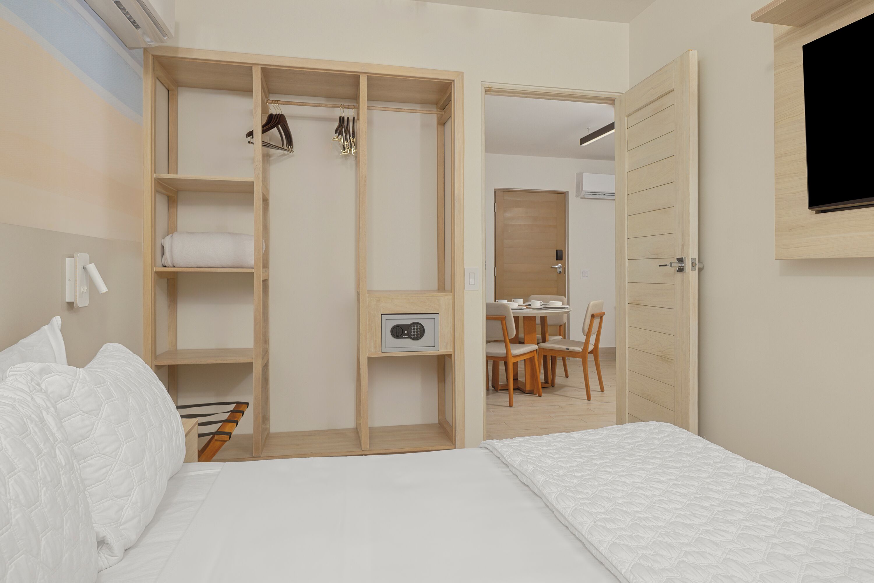 A bedroom with a bed, a wooden wardrobe, and a desk with chairs.