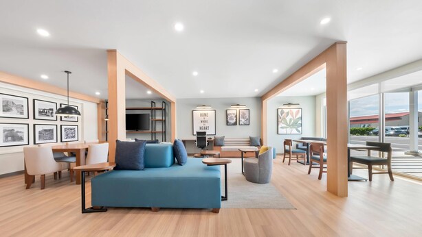 A modern living room with a blue sofa, wooden flooring, and framed pictures on the walls. - Everhome Suites Amarillo West - Medical Center (Amarillo)