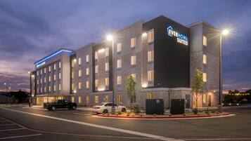 A modern hotel with multiple floors, a parking lot, and a well-lit entrance.