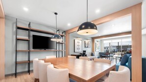 A modern dining area with a wooden table and chairs, a television on a wall, and a view of the outside. - Everhome Suites Amarillo West - Medical Center (Amarillo)