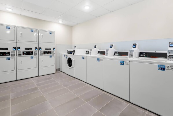 A commercial laundry facility with multiple washing machines and dryers, each with control panels and numbered for identification.