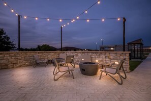 An outdoor patio area with stone walls, lounge chairs, and a fire pit, illuminated by string lights. - Everhome Suites Amarillo West - Medical Center (Amarillo)