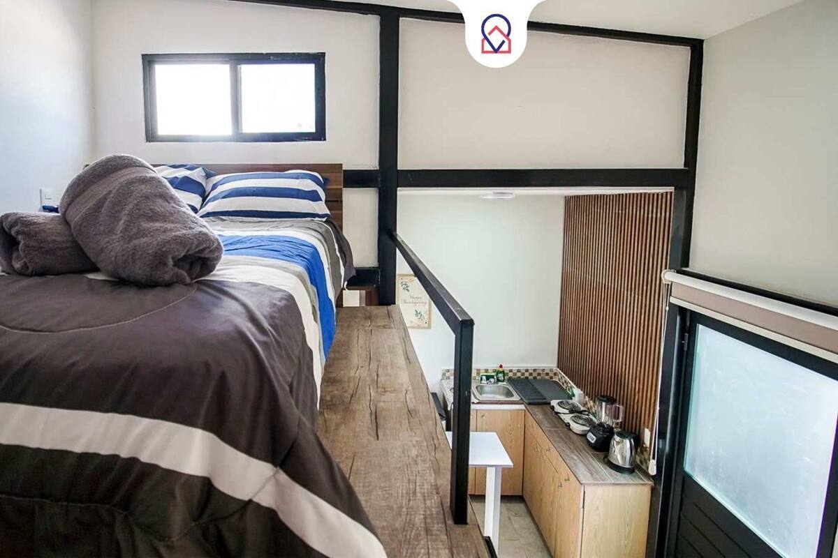 A hotel room with a bed, a small table with kitchen items, a window, and a view of the outside.