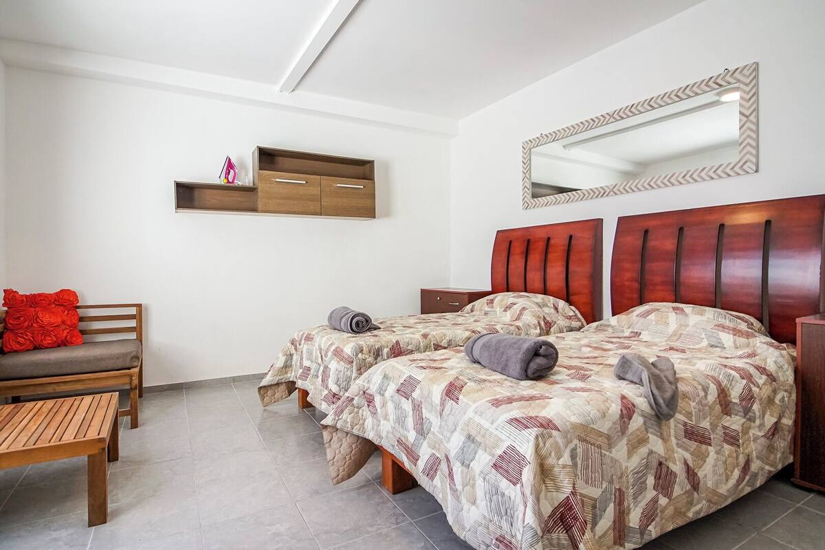 A bedroom with two beds, a wooden bench, a small table, and a nightstand.