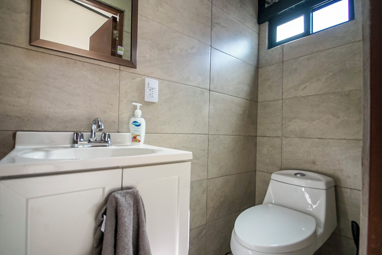 A bathroom with a white sink, a mirror, a toilet, and a towel hanging on the wall.
