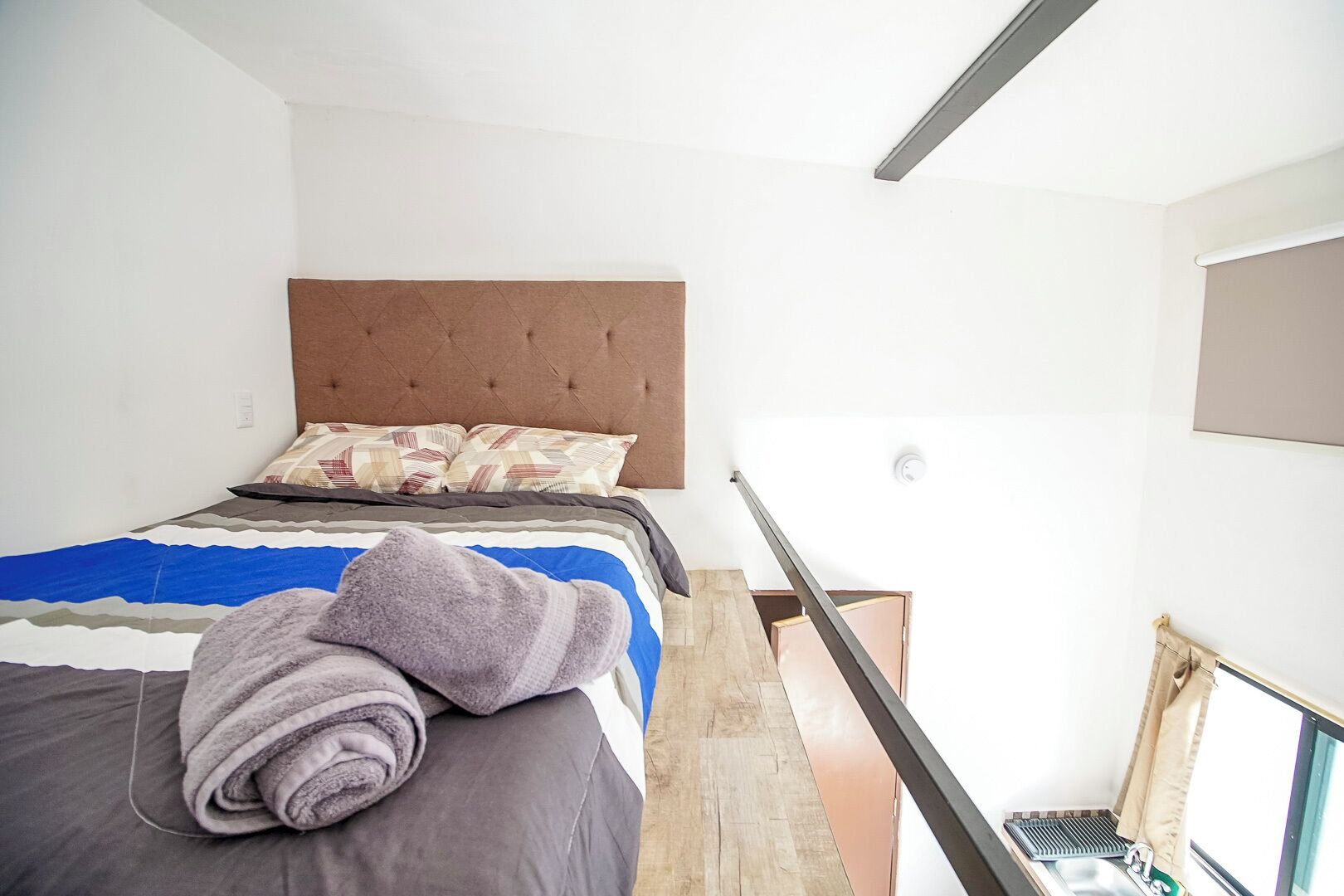 A bedroom with a bed, a headboard, a window, and a view of the outside.