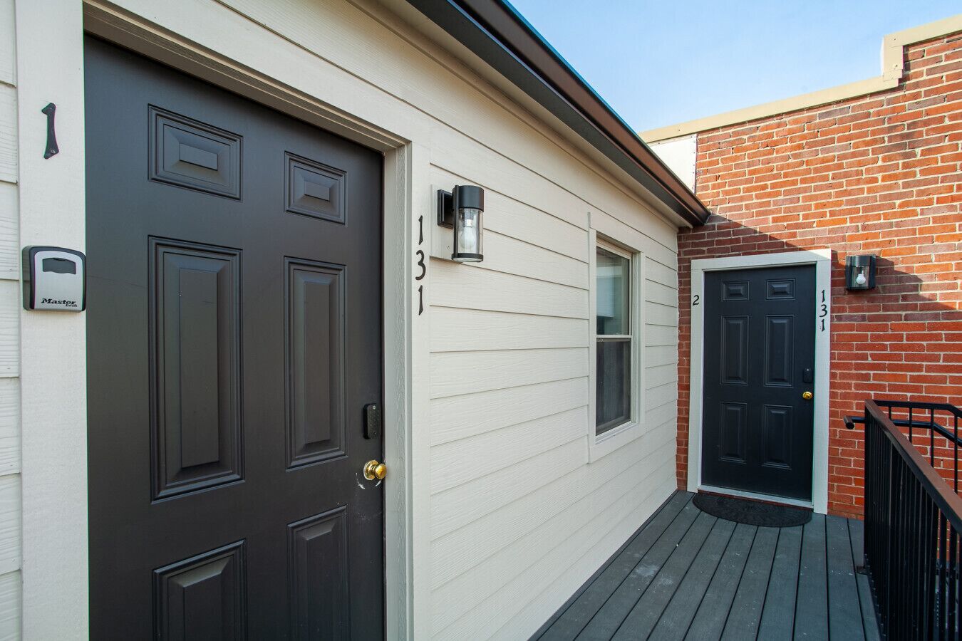 A two-story house with a dark brown front door, a white front door, and a brick side wall.