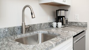 Una cocina con un lavamanos de acero inoxidable, un grifo moderno, una cafetera y dos tazas blancas sobre la encimera.