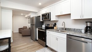 Una cocina moderna con armarios blancos, electrodomésticos de acero inoxidable, una encimera de mármol y una zona de comedor con mesa y sillas.
