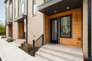 A modern apartment building with a wooden facade, a black door, and a small porch with steps.