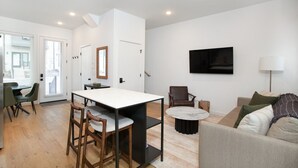 Een moderne woonkamer met een bank, een salontafel en een televisie. Er is een eethoek met een tafel en stoelen.